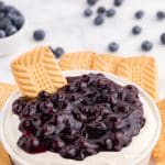 a shortbread cooking stuck in the center of a bowl of blueberry cheesecake dip