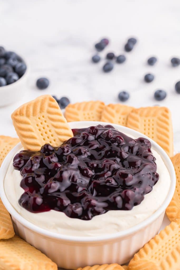 a shortbread cooking stuck in the center of a bowl of blueberry cheesecake dip