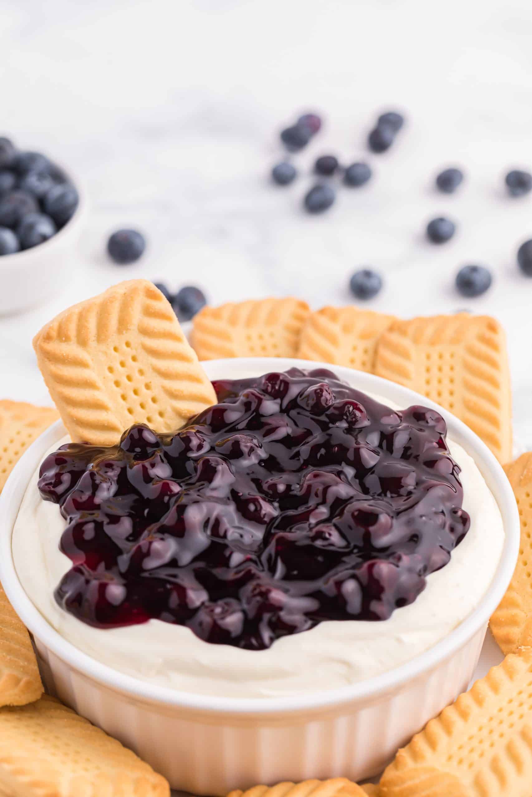 a shortbread cooking stuck in the center of a bowl of blueberry cheesecake dip