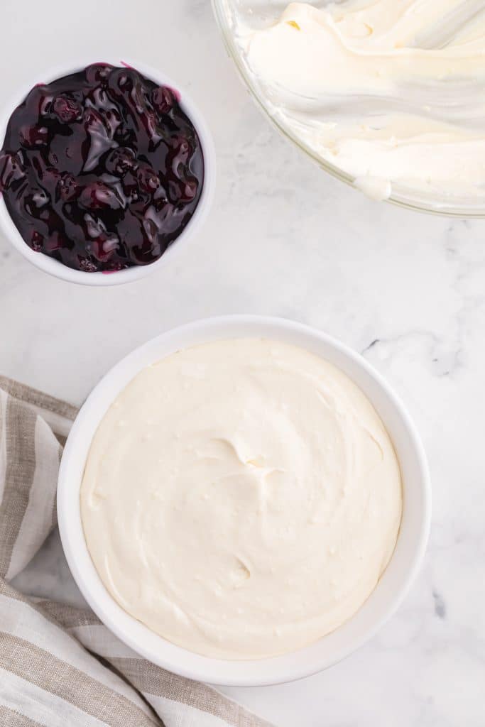 cheesecake dip in a small white bowl with a bowl of blueberry pie filling on the side