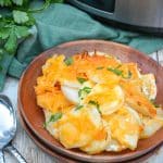 cheesy crockpot scalloped potatoes on a wooden plate in front of a silver slow cooker