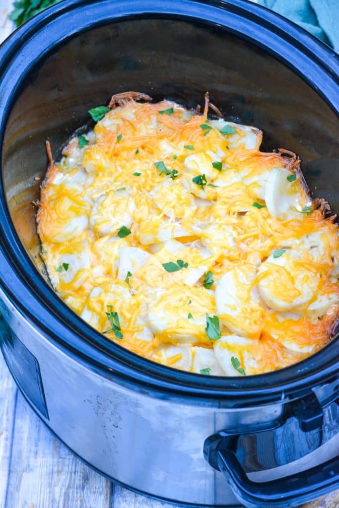 cheesy scalloped potatoes in the bowl of a black crockpot