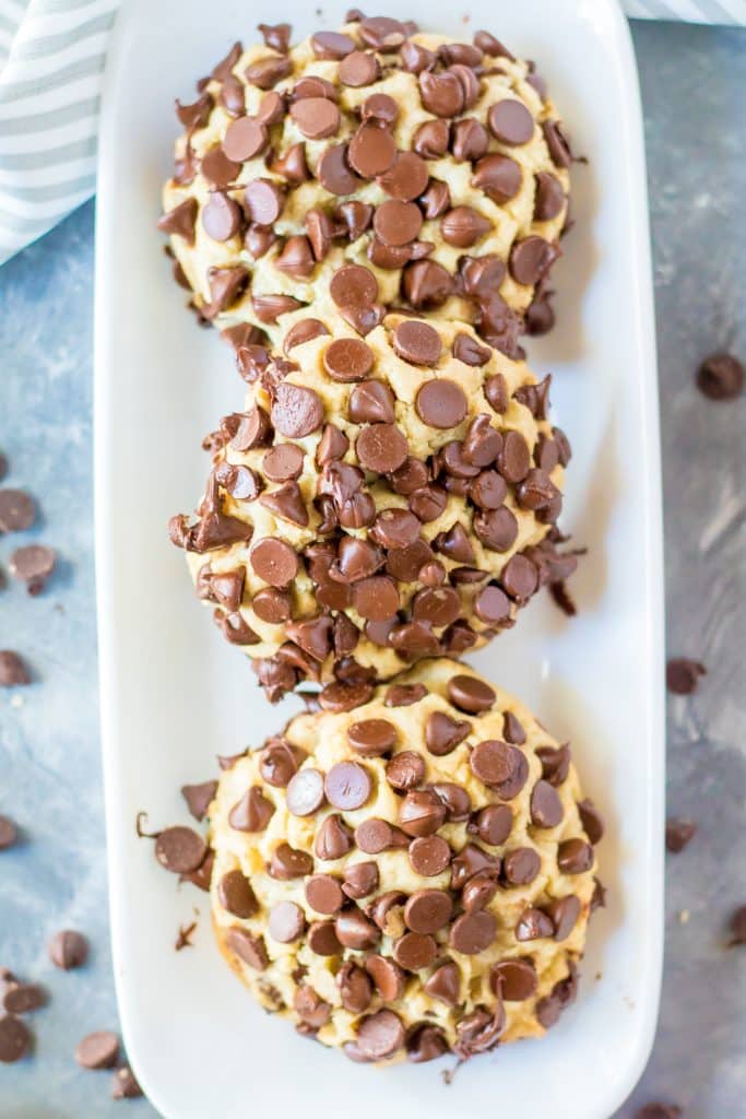 three giant chocolate chip cookies arranged in a row on a narrow white serving dish