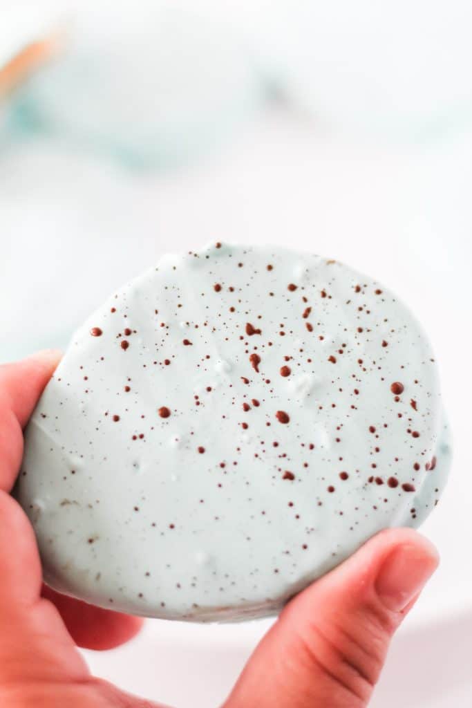 a hand holding up a speckled blue chocolate coated peanut butter egg