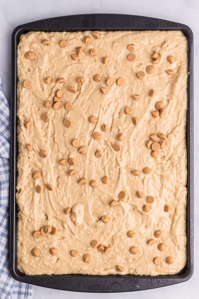 sheet pan peanut butter pancake batter spread out in a large rimmed baking sheet and topped with peanut butter baking chips