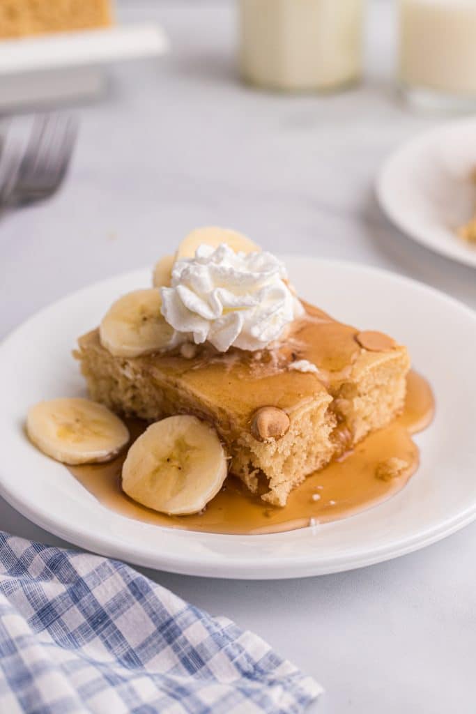 a peanut butter pancake slice on a white plate topped with syrup, sliced bananas, and a dollop of fluffy whipped cream