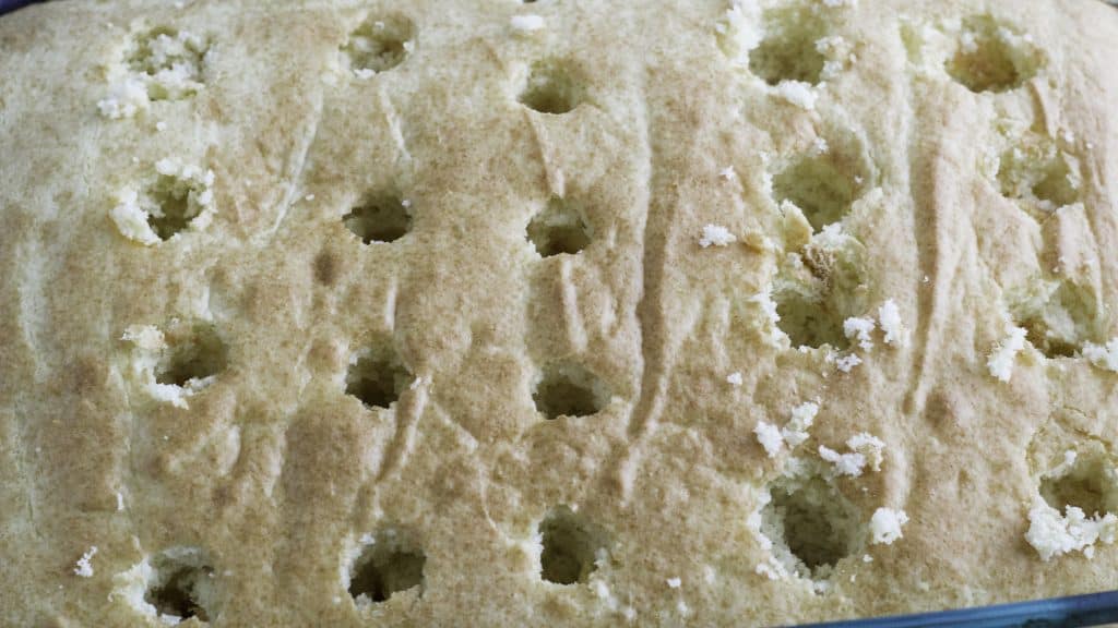a white cake with large holes poke all over the surface