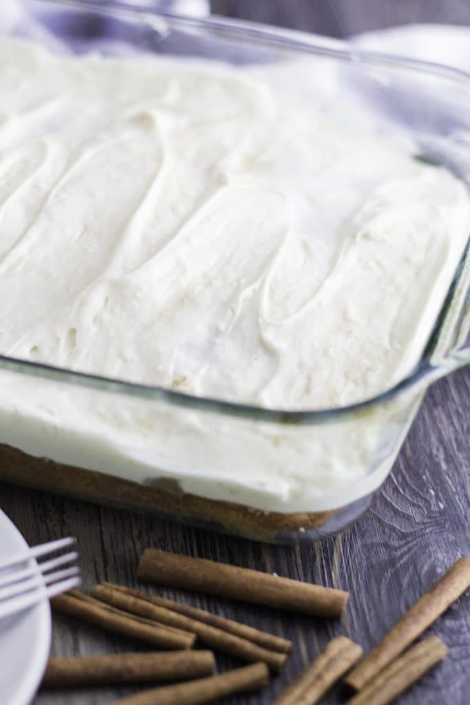 a cinnamon roll poke cake spread with fluffy whipped cream cheese frosting in a glass baking dish