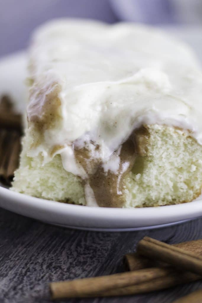 a slice of cinnamon roll poke cake on a white plate with a fork on the side