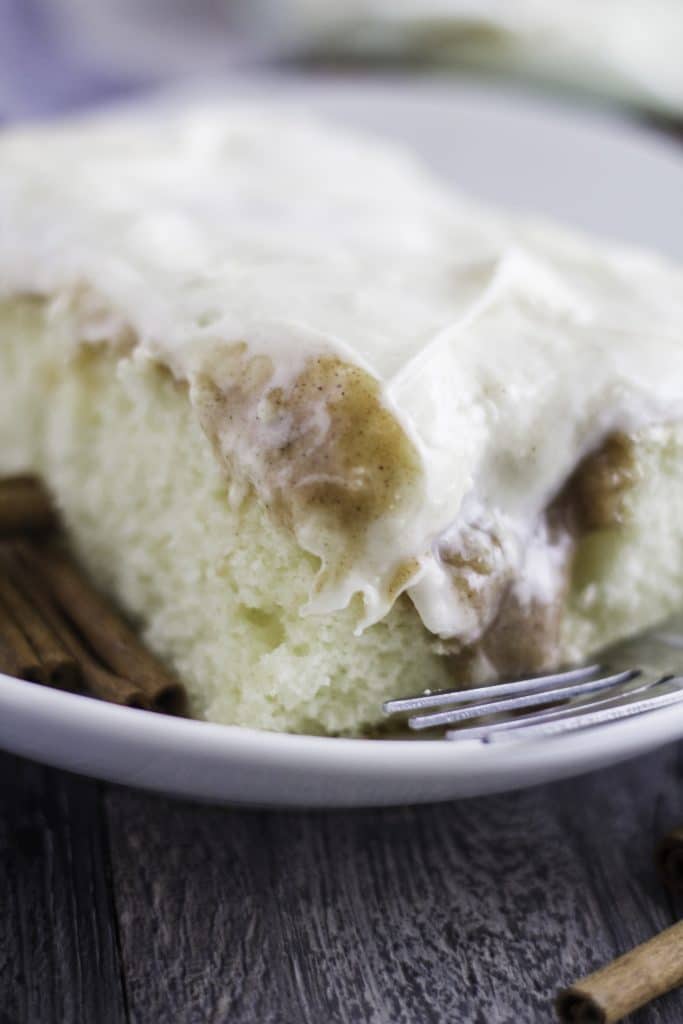 a slice of cinnamon roll poke cake on a white plate with a fork on the side