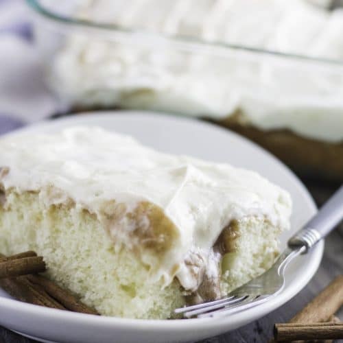 a slice of cinnamon roll poke cake on a white plate with a fork on the side