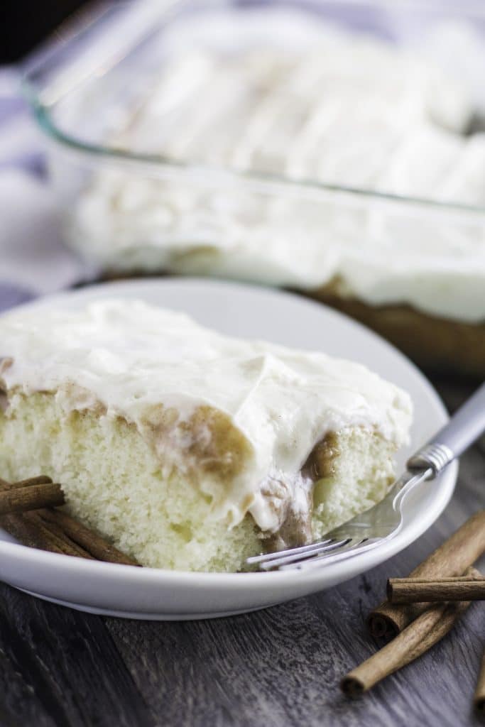 a slice of cinnamon roll poke cake on a white plate with a fork on the side