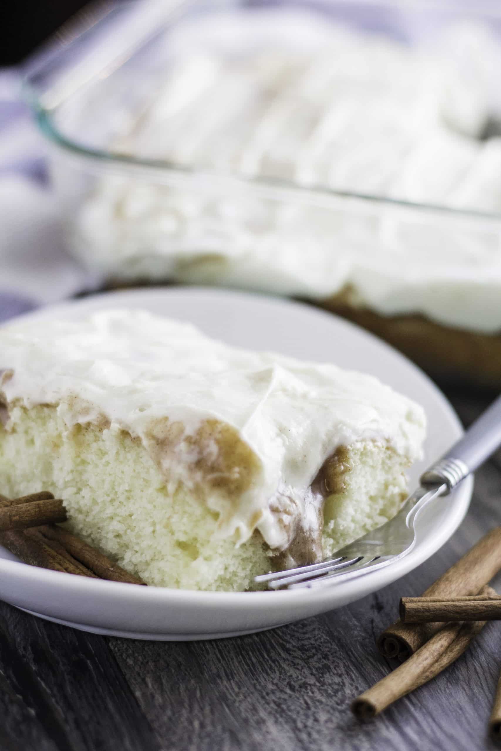 a slice of cinnamon roll poke cake on a white plate with a fork on the side