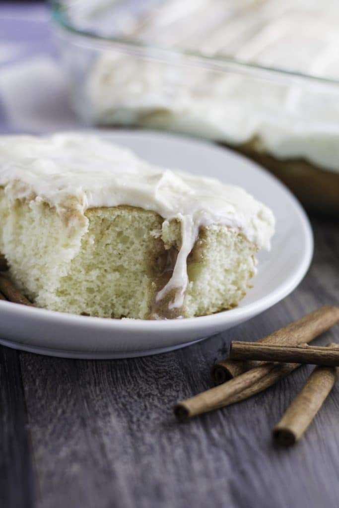 a slice of cinnamon roll poke cake on a white plate with a fork on the side
