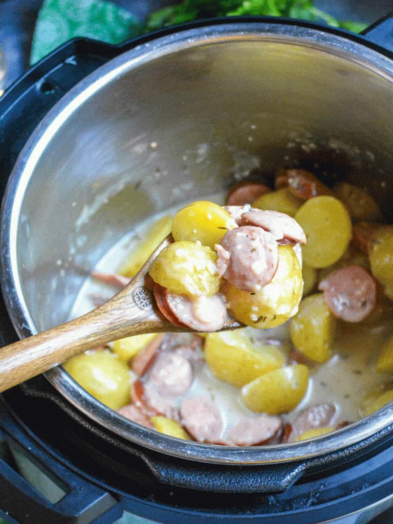 a wooden spoon holding a scoop of creamy potatoes and sausage over the bowl of an instant pot