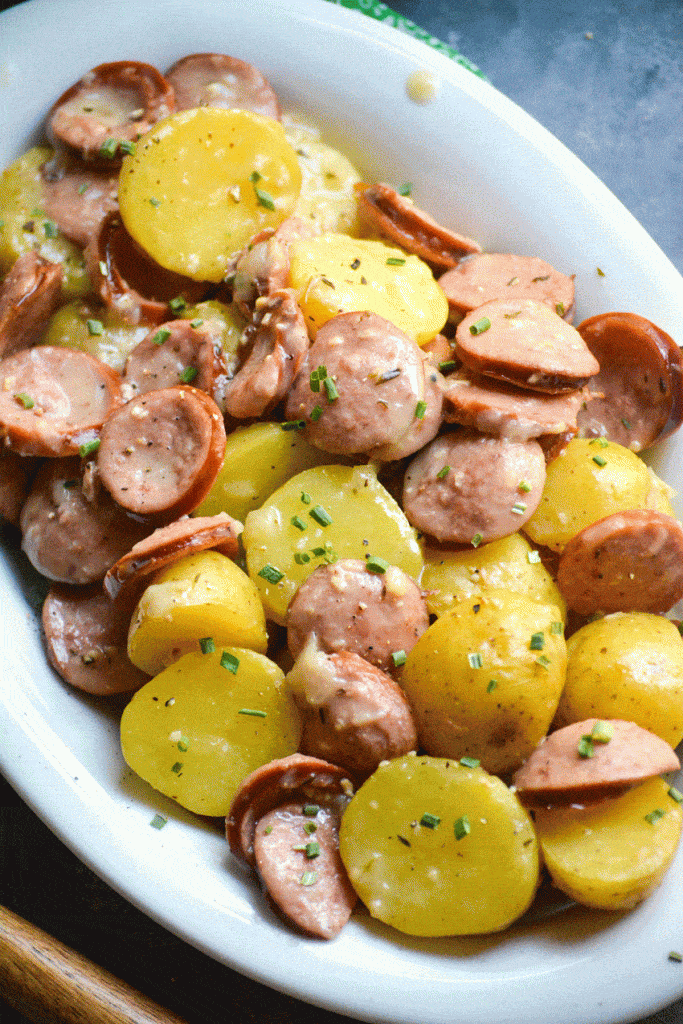 Instant pot creamy kielbasa and potatoes in a white serving platter with a bowl of shredded Parmesan cheese on the side