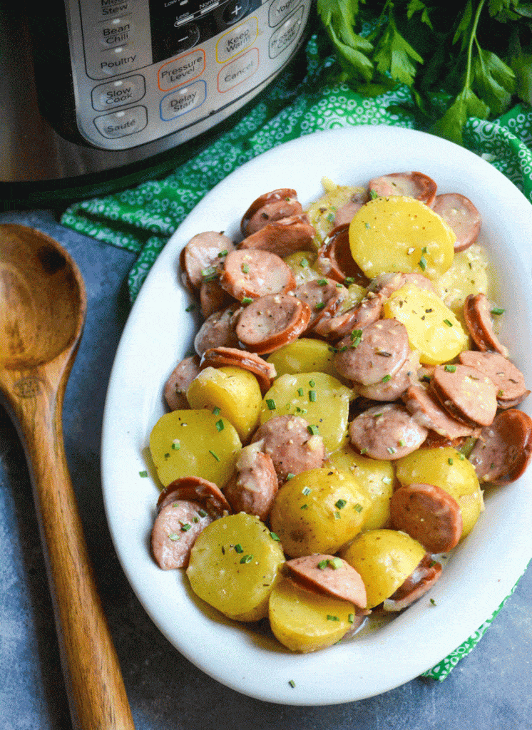Instant pot creamy kielbasa and potatoes in a white oval serving bowl with a wooden spoon on the side