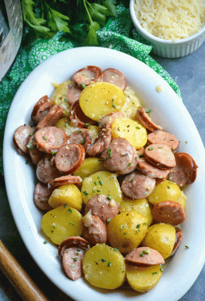 Instant pot creamy kielbasa and potatoes in a white serving platter with a bowl of shredded Parmesan cheese on the side