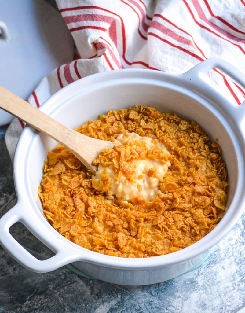 a wooden spoon in a white casserole dish filled with Instant Pot funeral potatoes