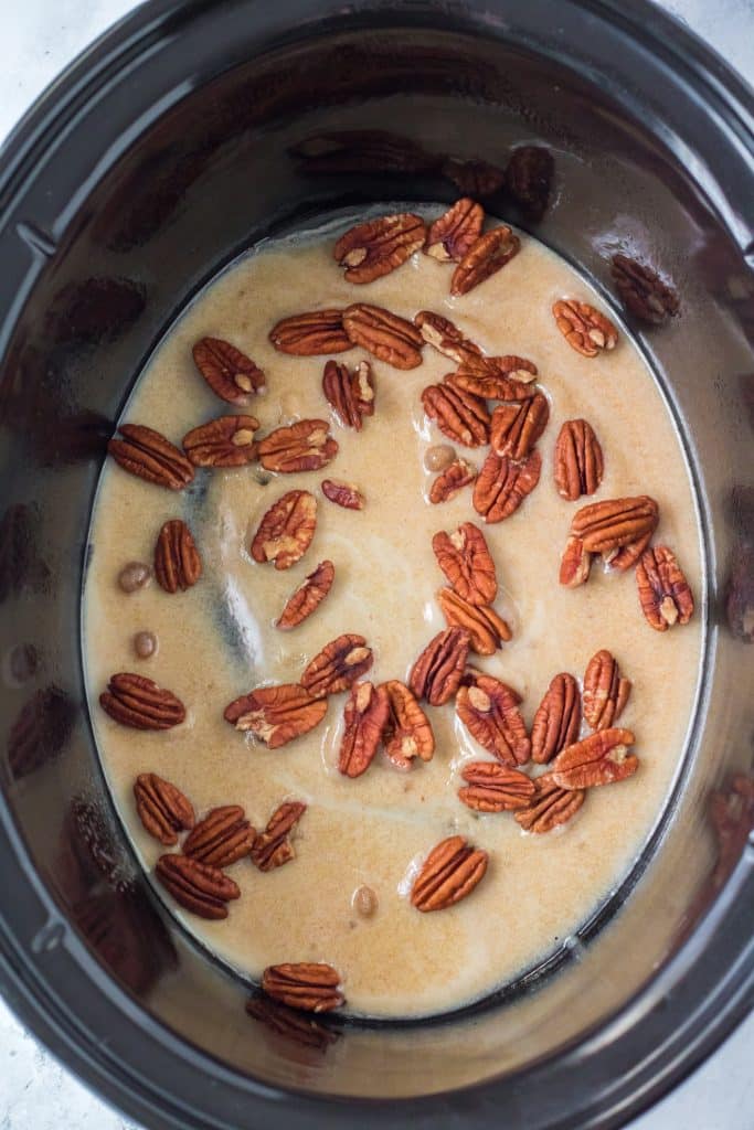 pecans in a brown sugar butter sauce on the bottom of a black crockpot