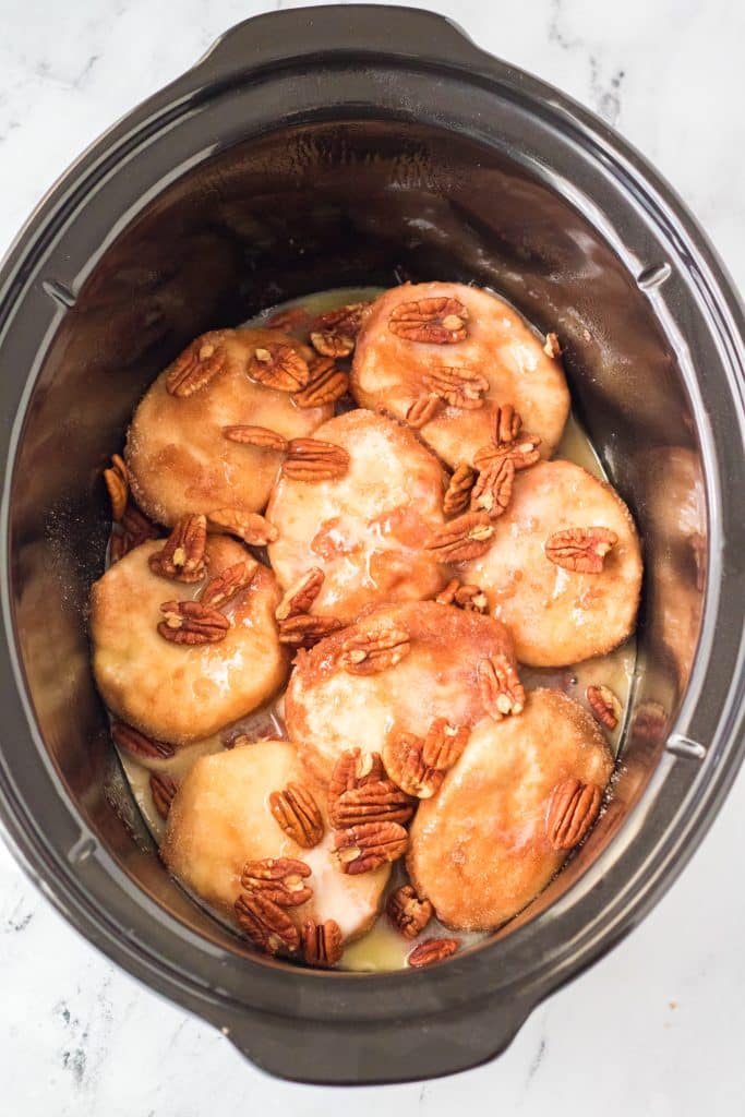 canned biscuits and pecans layered in a black crockpot and drizzled with brown sugar butter