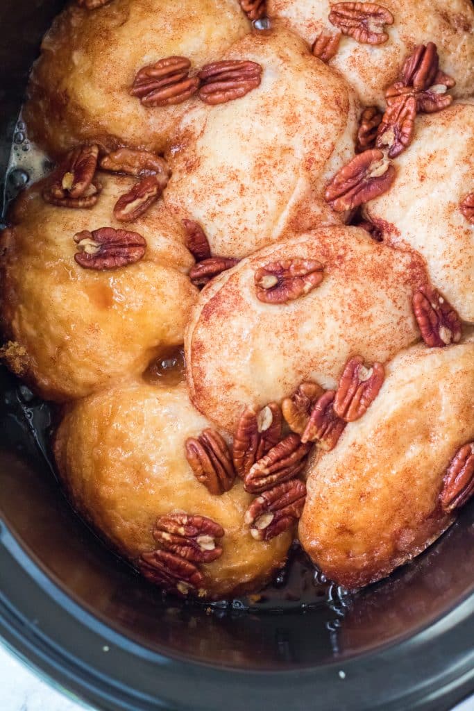 canned biscuits and pecans layered in a black crockpot and drizzled with brown sugar butter