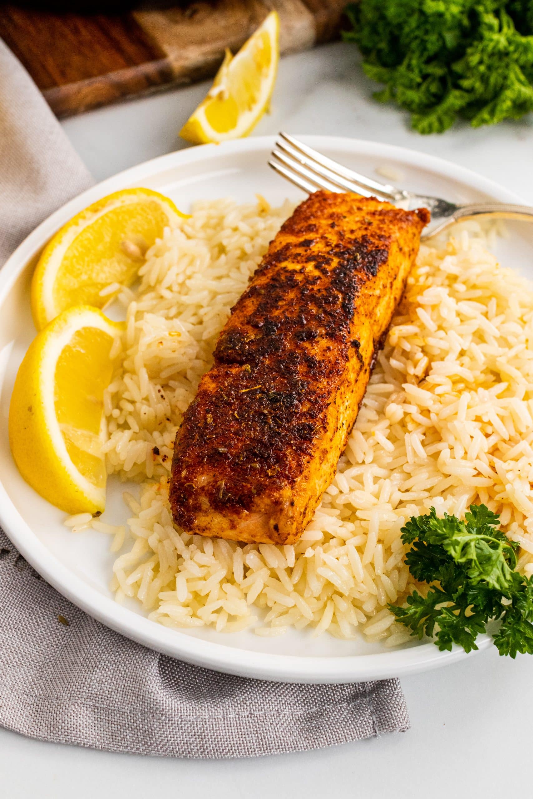 Blackened Salmon Recipe a blackened salmon filet on a bed of white rice next to lemon wedges on a white plate