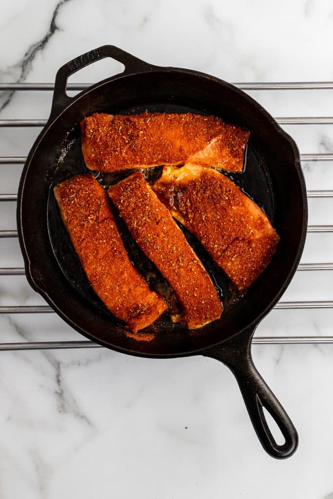 seasoned salmon filets in a black cast iron skillet set on a wire rack