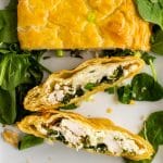 Greek chicken and spinach pie with puff pastry sliced & served on a bed of spinach on a white platter