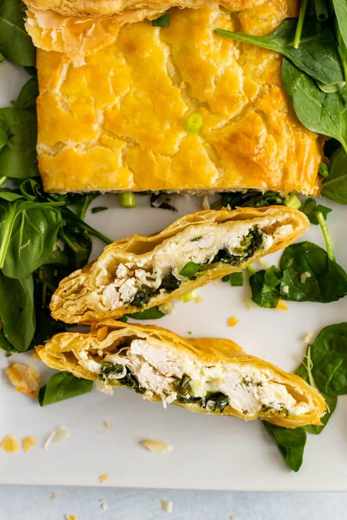Greek chicken and spinach pie with puff pastry sliced & served on a bed of spinach on a white platter