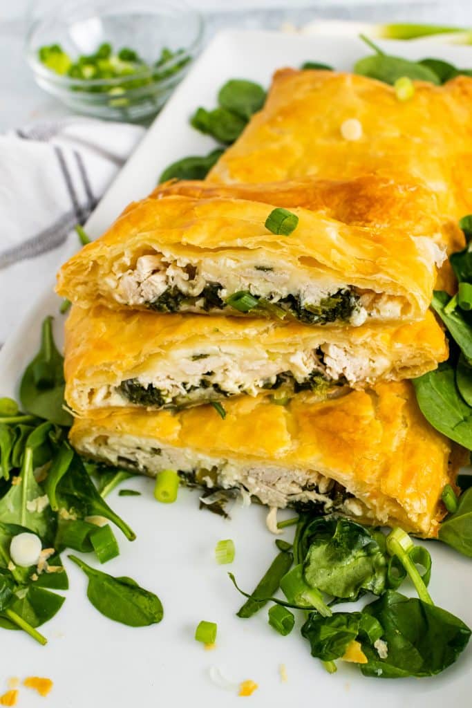 Greek chicken and spinach pie with puff pastry sliced & served on a bed of spinach on a white platter