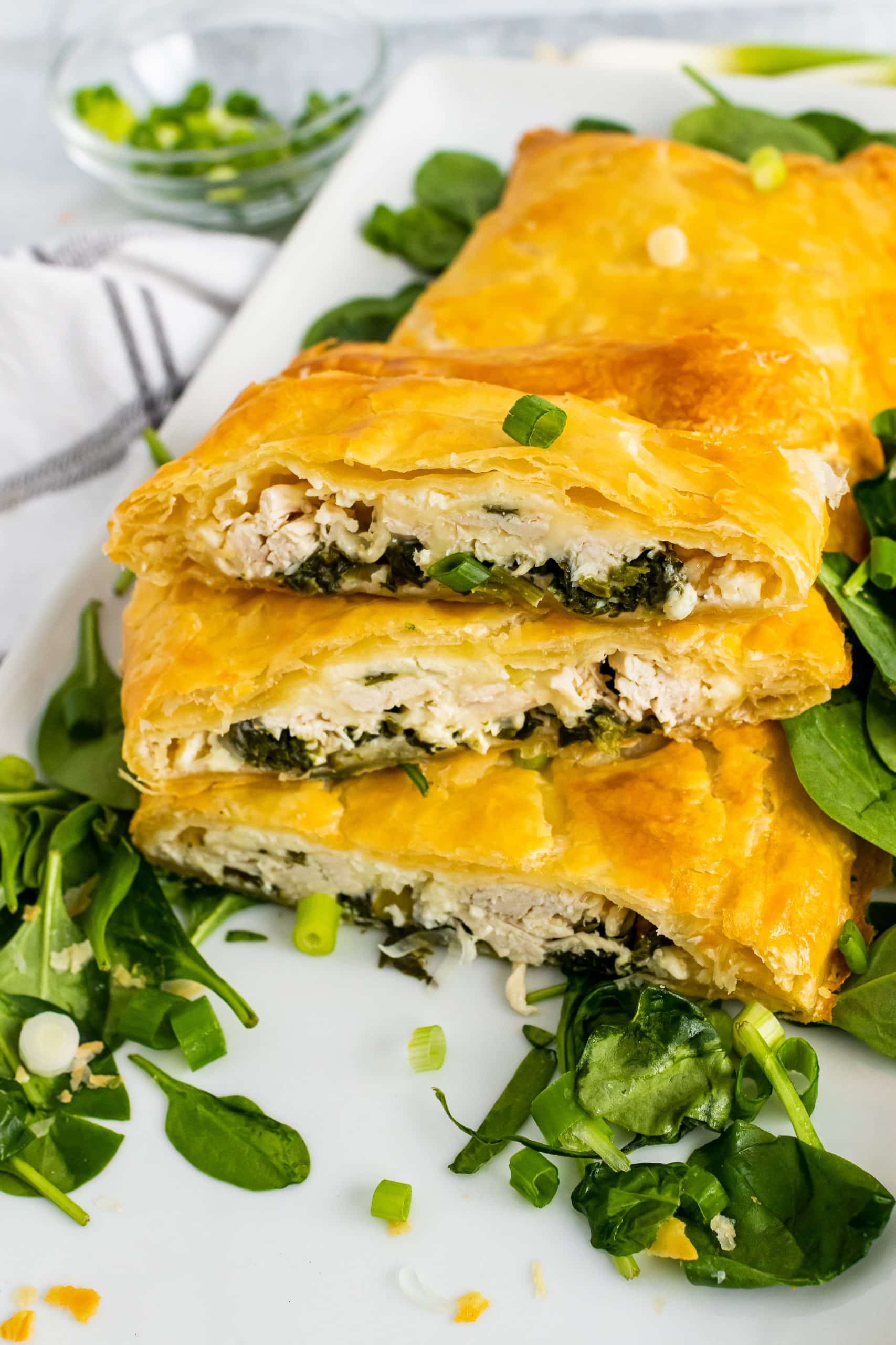 Greek Spinach And Chicken Pie Greek chicken and spinach pie with puff pastry sliced & served on a bed of spinach on a white platter