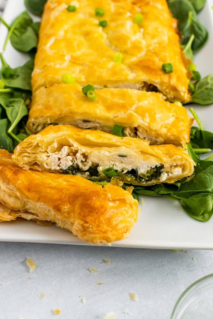 slices of greek chicken and spinach pie on a white serving platter with fresh spinach leaves on the sides