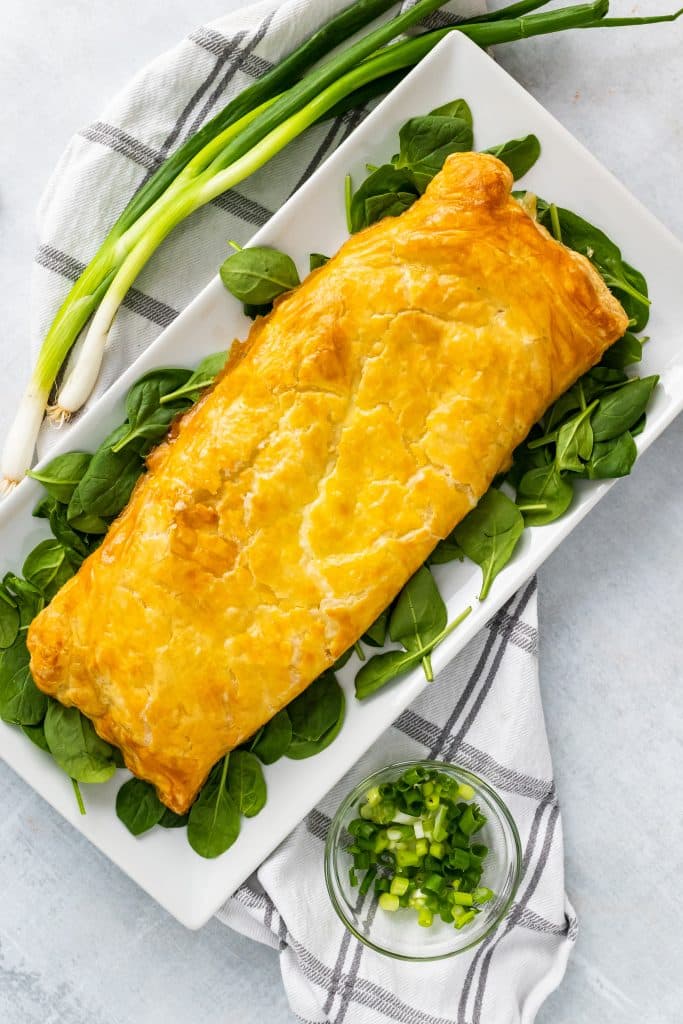 golden brown, crisp greek chicken and spinach pie on a bed of spinach on a white serving platter
