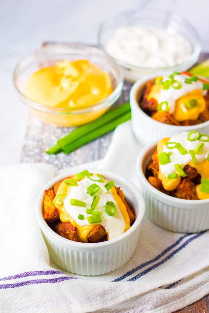 cheesy fiesta potatoes topped with sour cream and sliced green onions in small white ramekins