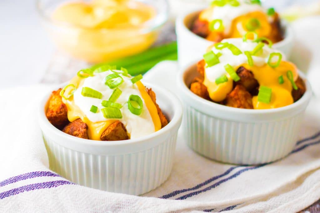 cheesy fiesta potatoes topped with sour cream and sliced green onions in small white ramekins
