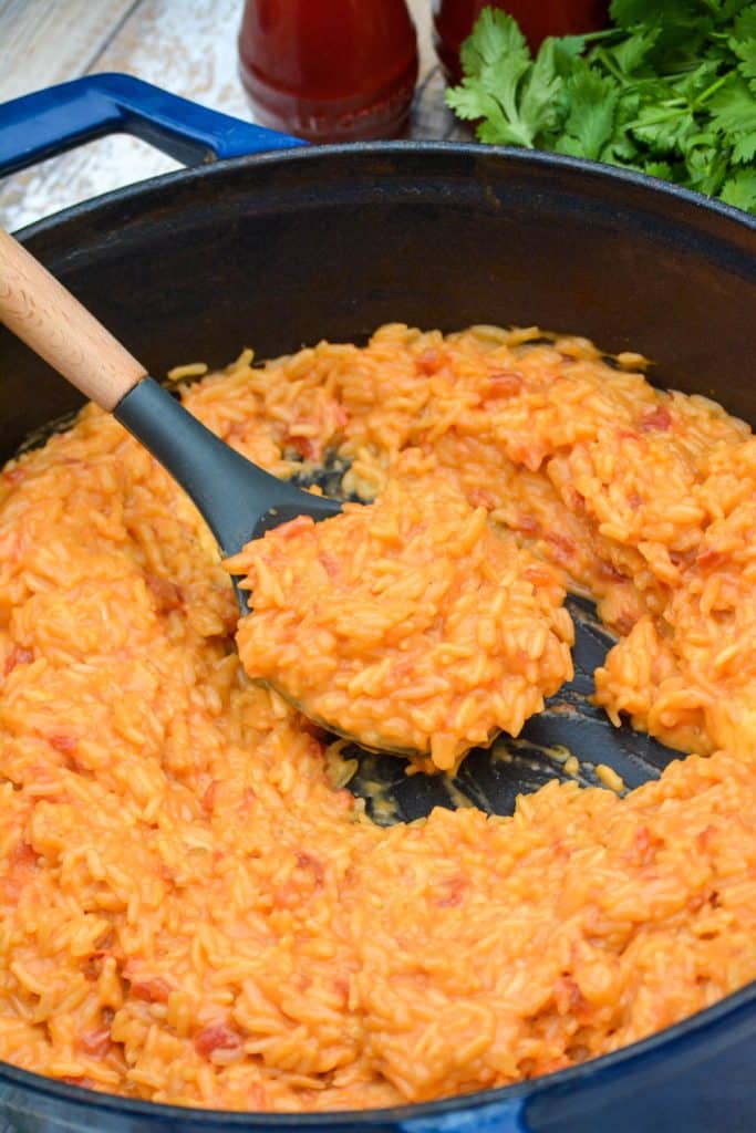 a wooden handled serving spoon in a skillet of cheesy queso rice