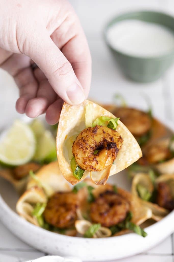a hand holding up a shrimp taco bite above a white plate
