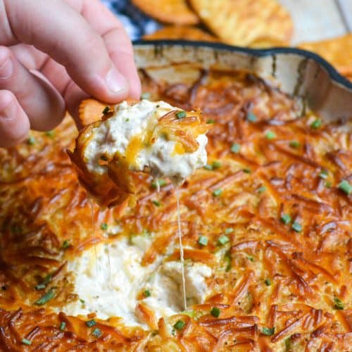 a hand lifting up a cracker covered in simple smoked crap dip