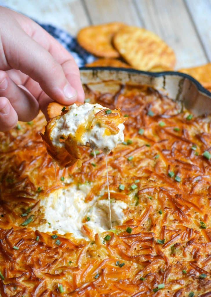 a hand lifting up a cracker covered in simple smoked crap dip