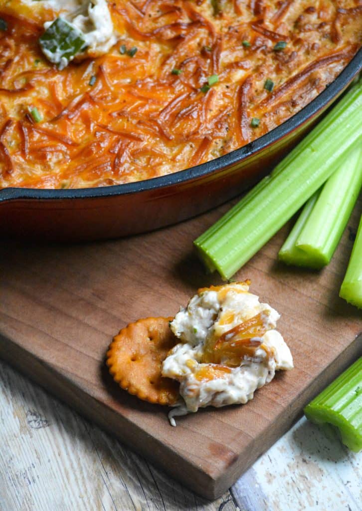 a cracker covered in a simple smoked crab dip sitting on a wooden cutting board