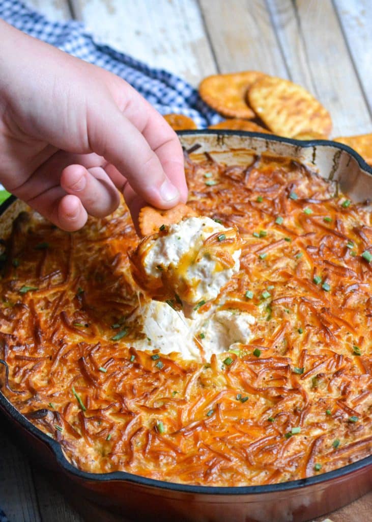a hand lifting up a cracker covered in easy smoked crap dip