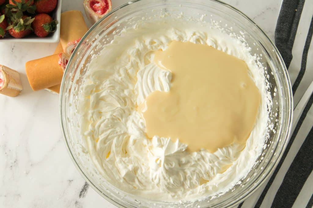 sweetened condensed milk added to a bowl of whipped cream