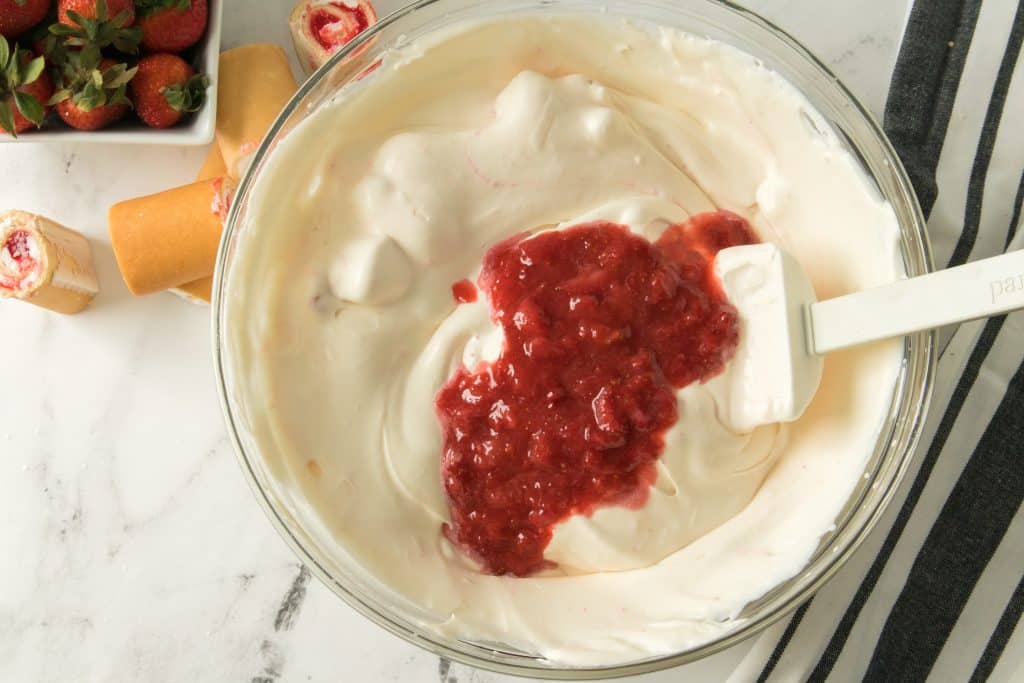 strawberry filling being added to a bowl of whipped cream