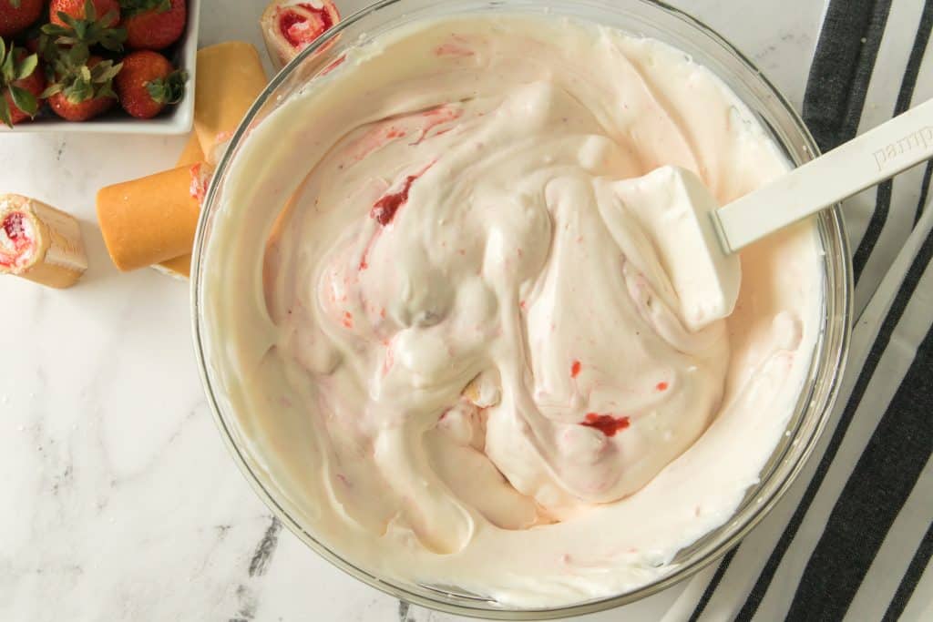 whipped cream and strawberry glaze mixed together by a white spatula in a glass mixing bowl