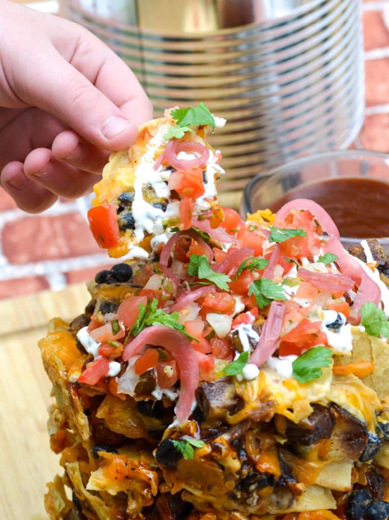 a hand holding up a loaded chip from a nacho stack