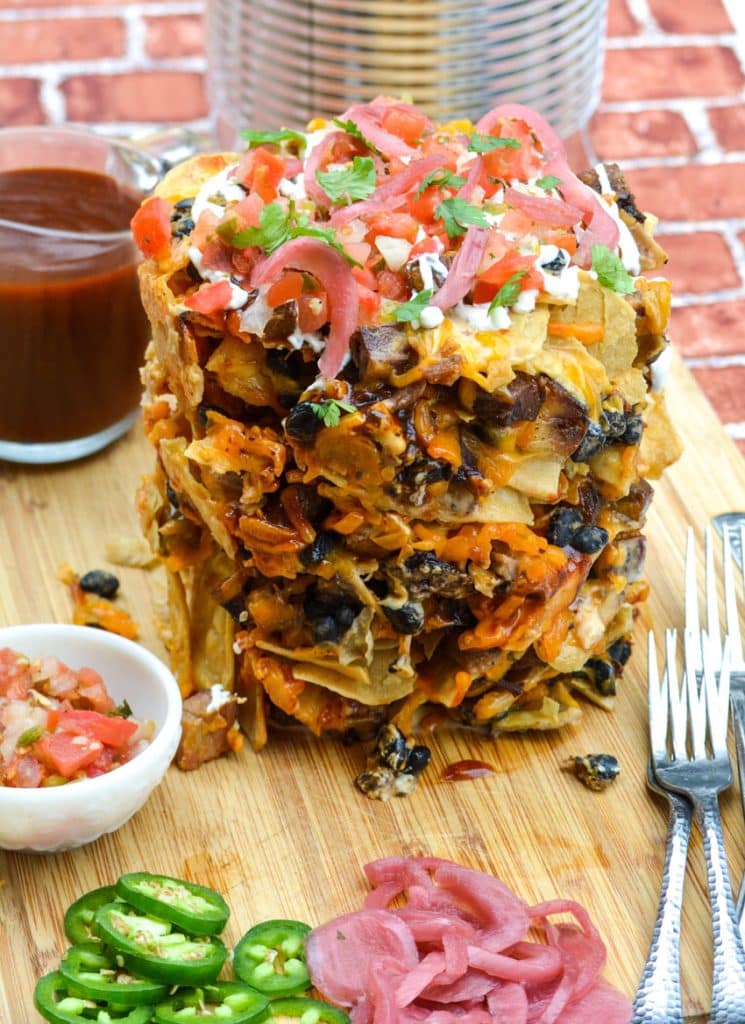 a stack of trash can nachos with beef brisket on a wooden cutting board
