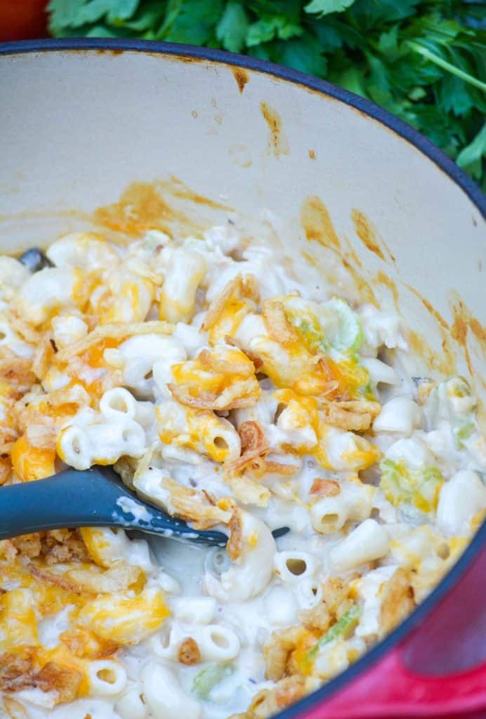a spoon scooping tuna melt macaroni and cheese from a red enameled cast iron dutch oven