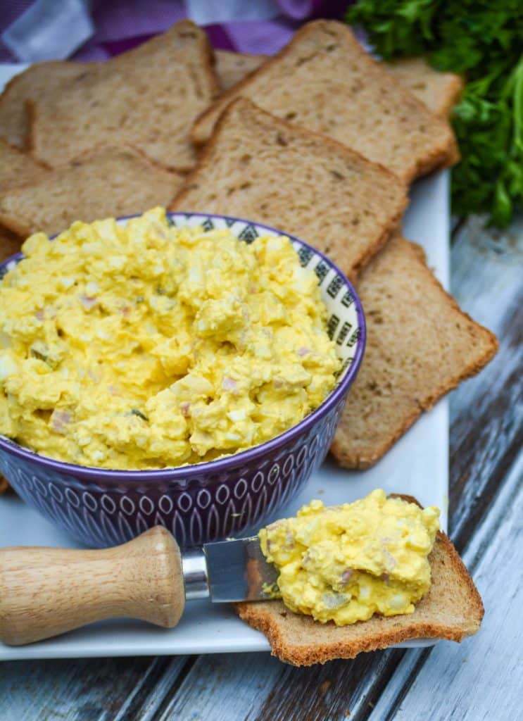 ham and egg salad being spread on a small slice of party toast on a white platter