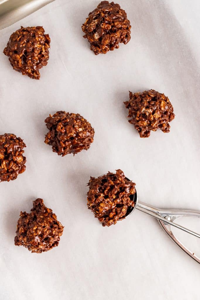 a metal cookie scoop spooning dollops of star crunch cookie mixture onto a parchment paper lined baking sheet